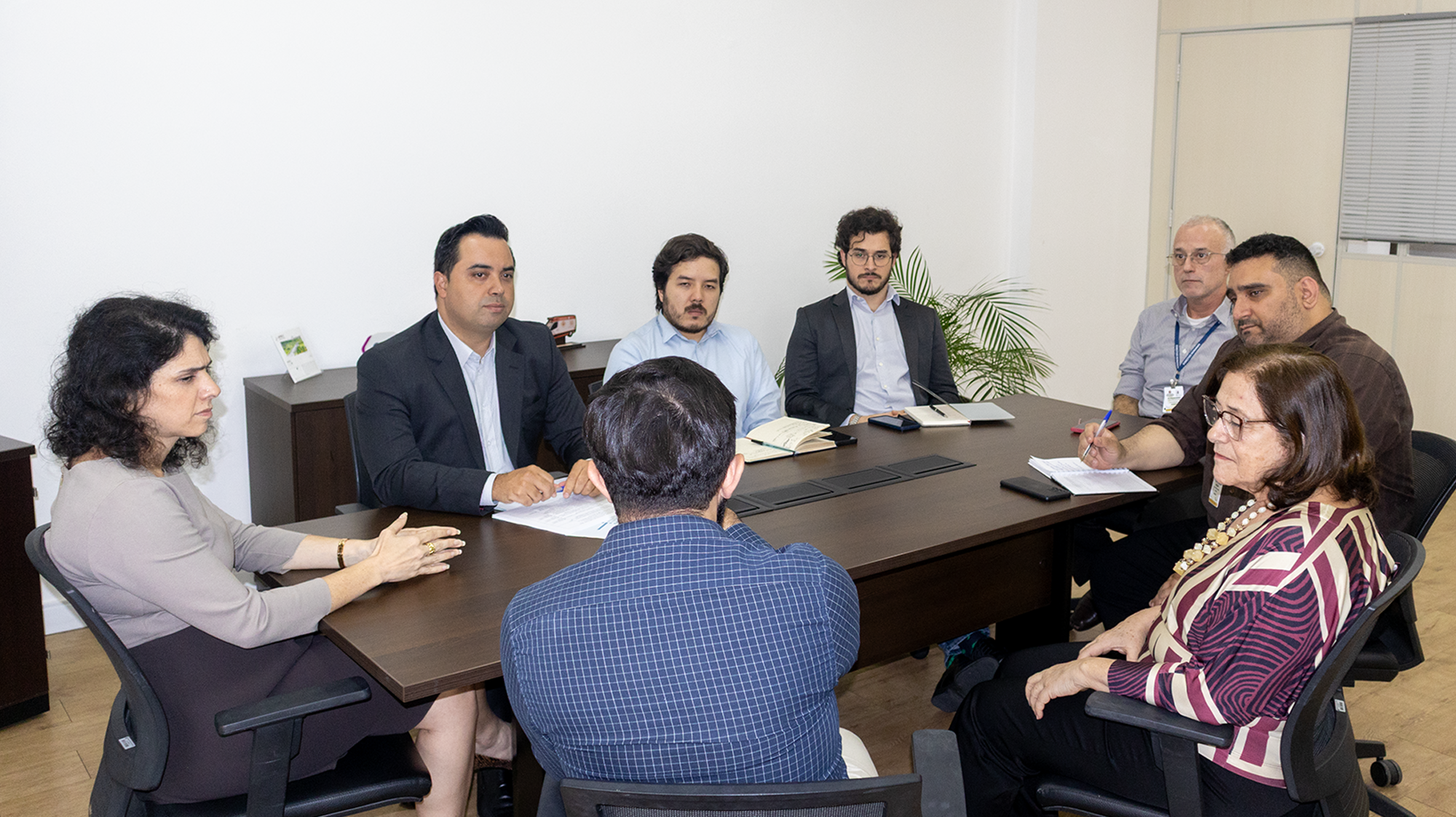 Foto de uma reunião com 8 pessoas dentro de uma sala