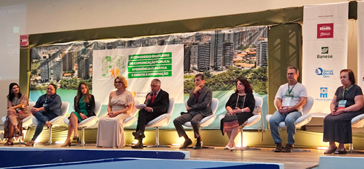 Foto de um palco com 9 pessoas. O ambiente é uma conferência