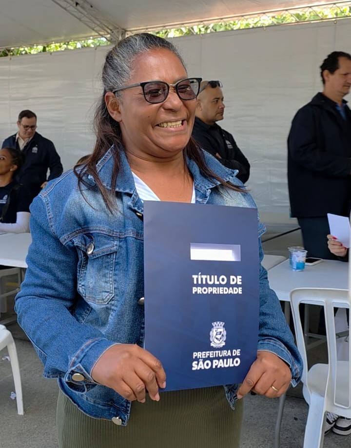 Mulher recebe título de propriedade de sua casa, em São Miguel Paulista, zona leste.