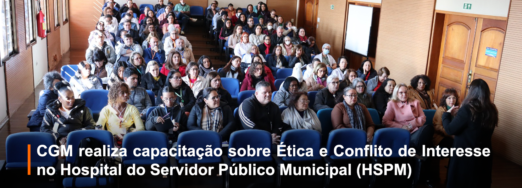 Baner de uma sala pequena com várias pessoas assistindo uma palestra