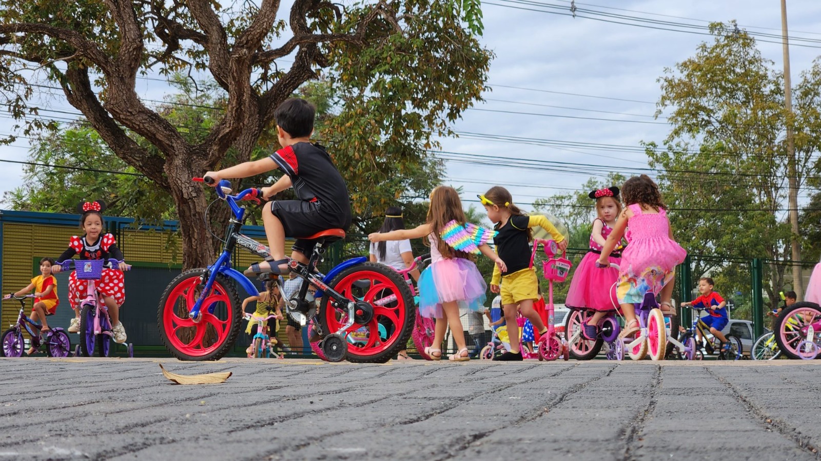 Na imagem, crianças fantasiadas andando de bicicleta.