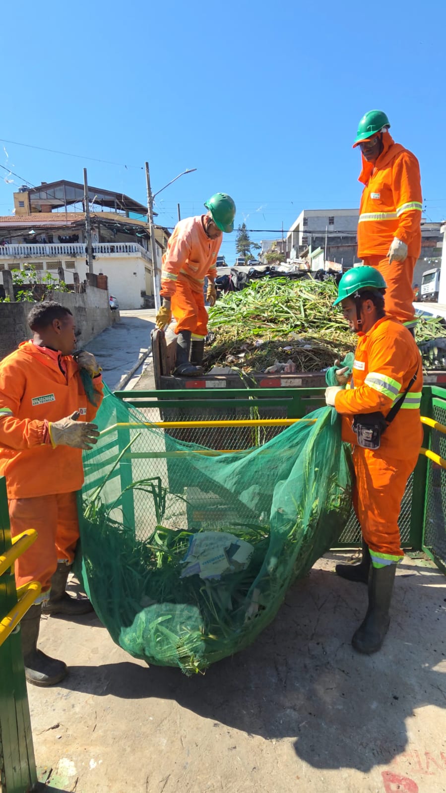 Equipes da Operação São Paulo Limpa realizam serviços de zeladoria urbana, recolhendo resíduos de poda e limpeza em via pública. Na imagem, trabalhadores uniformizados carregam sacos com vegetação e galhos para um caminhão de apoio, contribuindo para a conservação e manutenção dos espaços públicos da região.